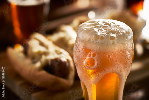 Φωτογραφία amber beer with overflowing foamy head and bratwursts in background