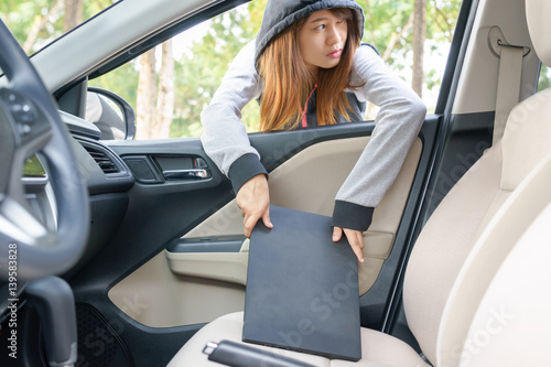 Woman burglar steal a laptop through the window of car - theft concept.