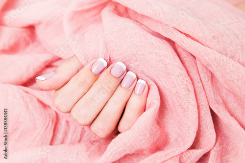 Close up of one female caucasian hand with beautiful pink french manicure isolated on fabric. Horizontal color photography.