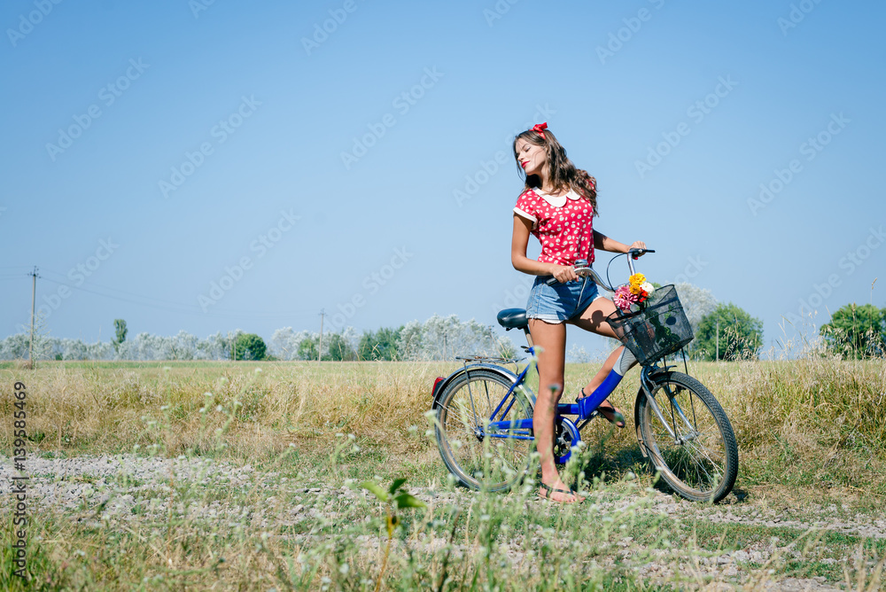 Joyful beautiful woman on a bicycle in the field landscape blue sky background outdoors