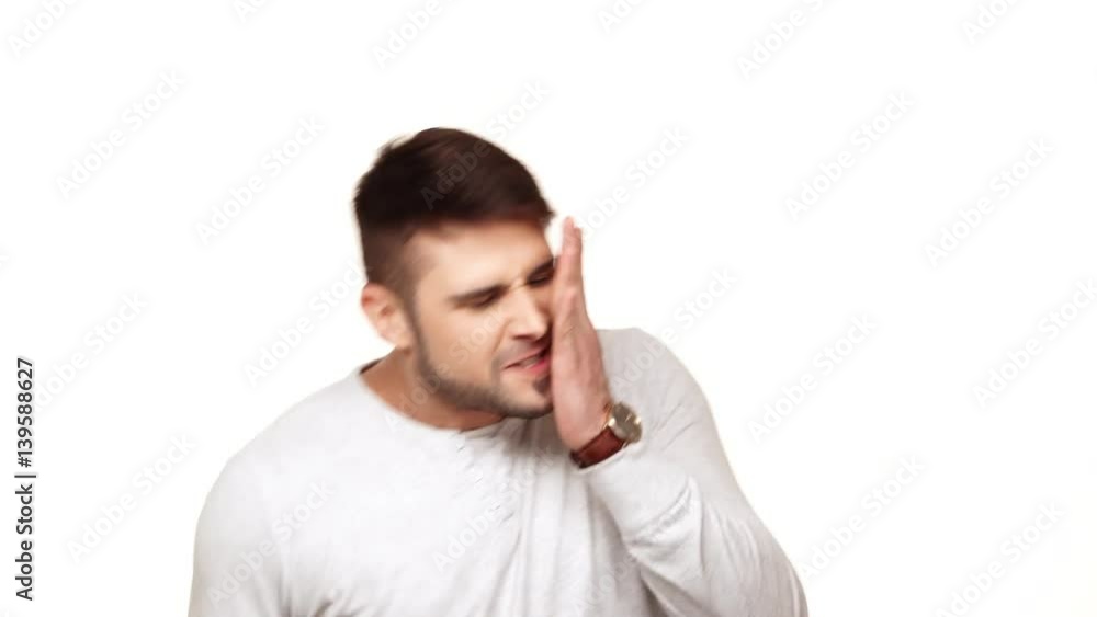 Concentrated tough guy in sweatshirt standing on white background trying to notice mosquito and hitting his check Concentrated tough guy in sweatshirt standing on white background trying to notice mosquito and hitting his check