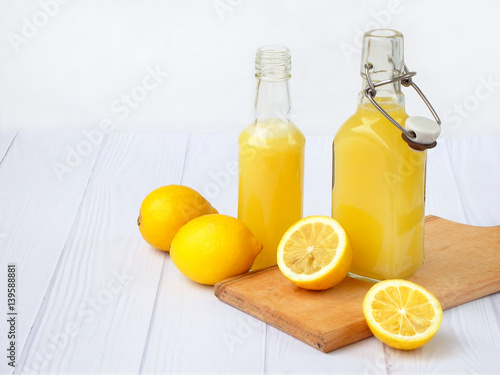 Freshly squeezed lemon juice in bottle and lemons on light background. For vitamin drink or cocktail. Selective focus. Space for text