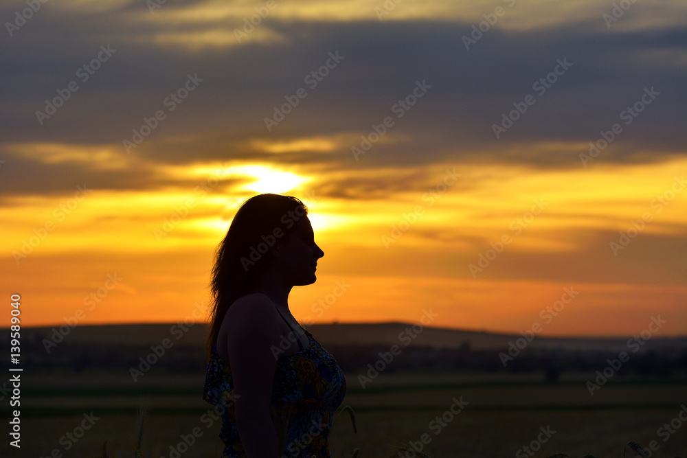 Silhouette of a young woman standing in dry grass field on sunset Silhouette of a young woman standing in dry grass field on sunset