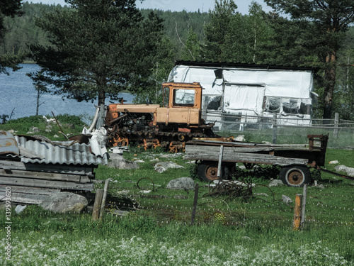 An old tractor with a cart stands on the grass in a village in Russia in the summer.