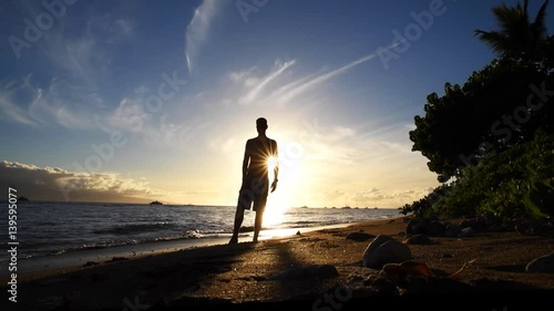 Silhouetted man doing yoga on tropical beach