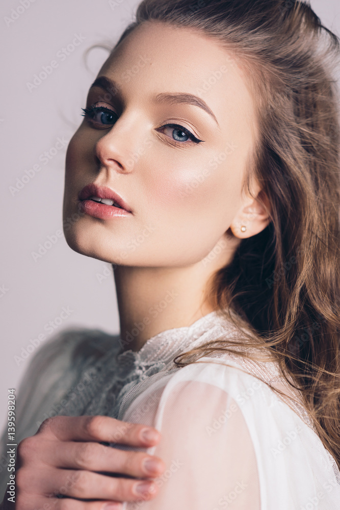© irinaneva - Portrait of a beautiful, gentle girl blonde in an image of the bride. Dressed in a light white lace dress. The beauty of the face. Photos in the studio on a gray background.