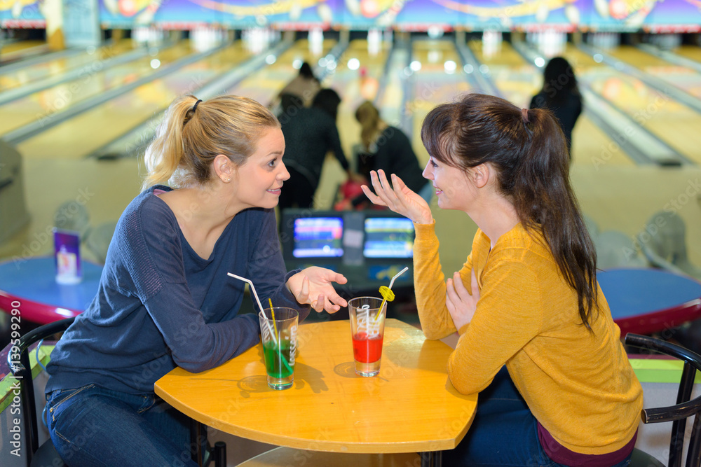 Woman sat at table chatting in bowling hall - obrazy, fototapety, plakaty 