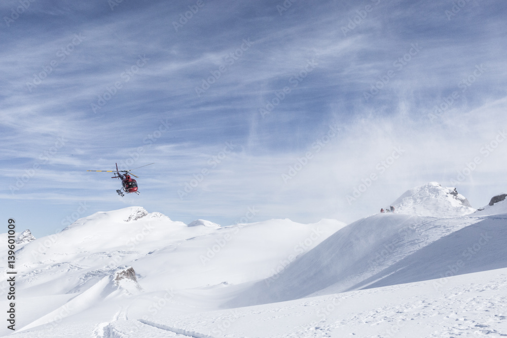 Helicopter fetching some skiers and snowboarders from a mountain next to the matterhorn in very high altitudes. Very good weather conditions, with snow flakes flying around caused by the chopper. 