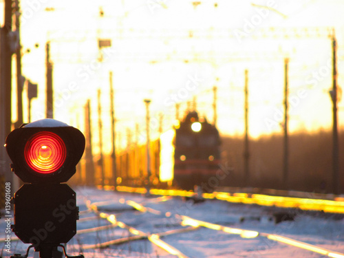 Railway traffic light shows blue signal on railway with blur effect and railway with freight train as the background during sunset.