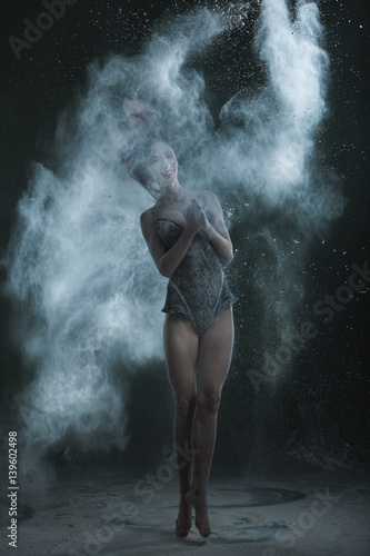 Woman dances in a cloud of dust from flour on a black background.