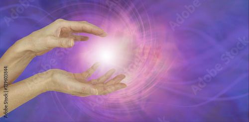 White Orb Energy Between Hands - a pair of female hands with a white energy orb between on an ethereal pink and purple vortexing energy field background 
