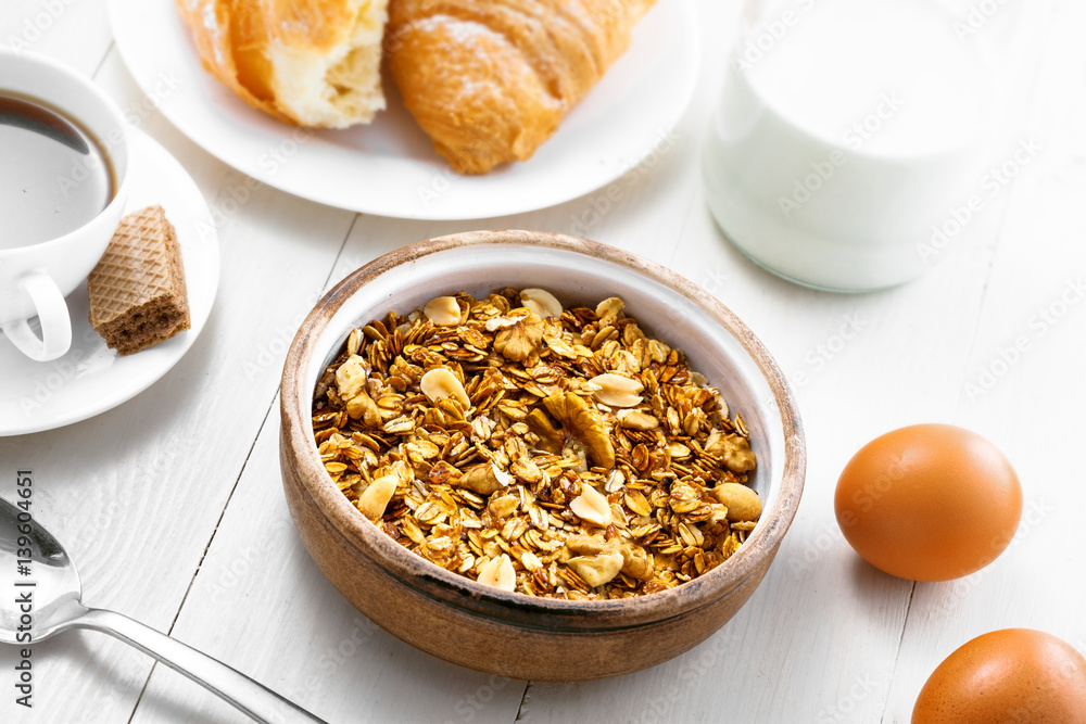Breakfast made of oatmeal granola, croissants, milk, eggs, coffee and fruits on a table. Delicious healthy food. Top view.