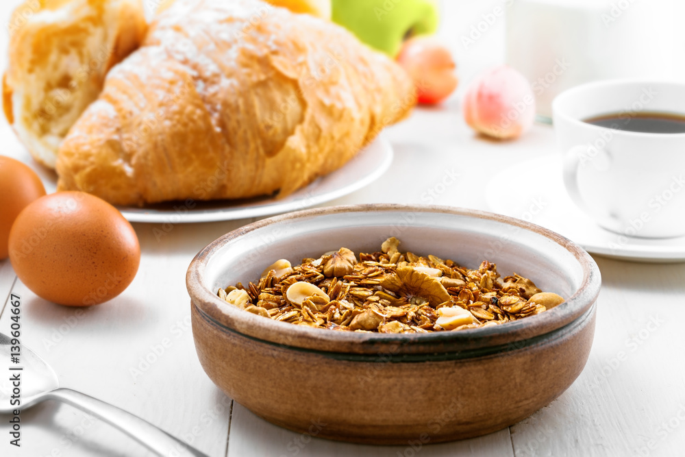 Oatmeal muesli with nuts, croissants, fruits, milk and coffee for delicious breakfast. Traditional healthy meal for breakfast on a table. Close-up. Oatmeal muesli with nuts, croissants, fruits, milk and coffee for delicious breakfast. Traditional healthy meal for breakfast on a table. Close-up.