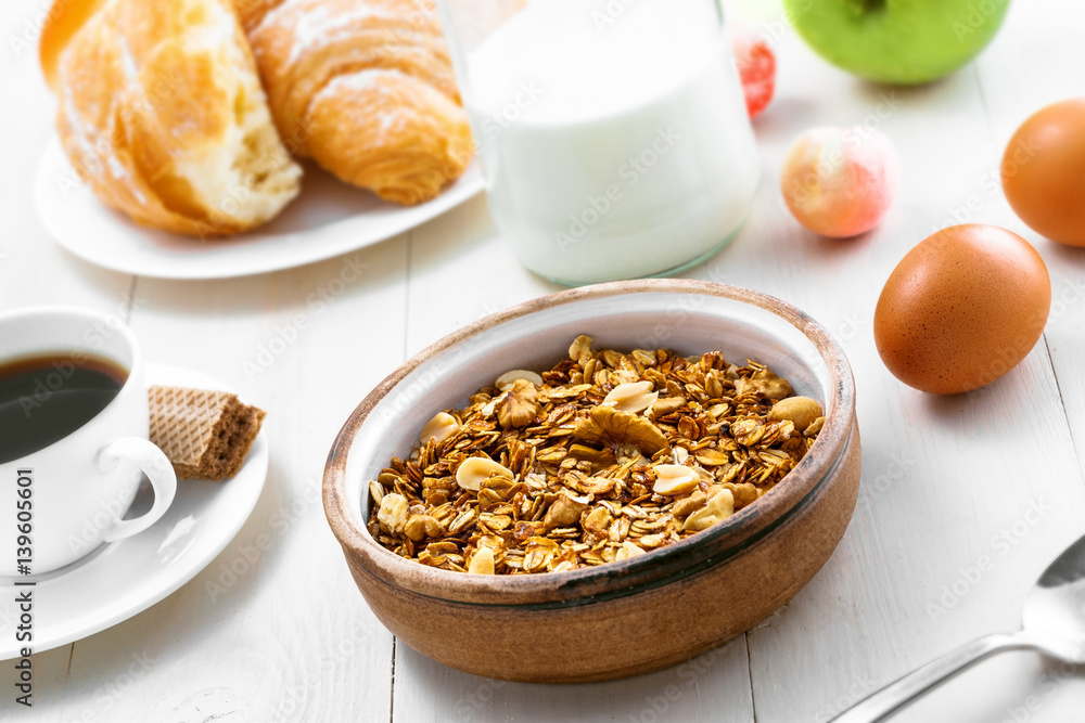 Healthy food for breakfast on a white wooden table. Oatmeal granola with nuts, coffee, croissants, eggs, milk and fruits for delicious healthy meal. Healthy food for breakfast on a white wooden table. Oatmeal granola with nuts, coffee, croissants, eggs, milk and fruits for delicious healthy meal.