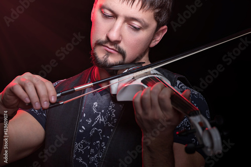 Young bearded man playing a white electric violin, isolated on a black background