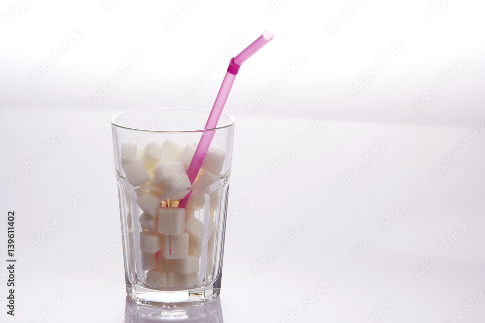 A glass filled with sugar cubes and a pink straw A glass filled with sugar cubes and a pink straw