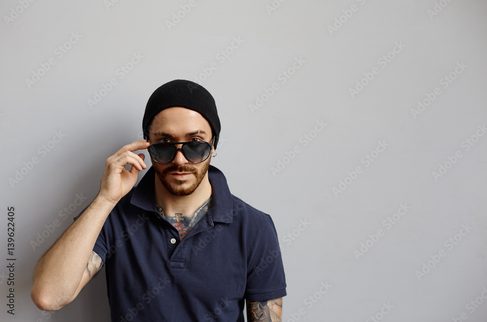 Macho brutal man with latin skin and tattooed hands portrait in studio on neutral fone. Strong and brave guy in sunglasses look to the camera,Copy space for pomotion content.Confident and calm emotion Macho brutal man with latin skin and tattooed hands portrait in studio on neutral fone. Strong and brave guy in sunglasses look to the camera,Copy space for pomotion content.Confident and calm emotion