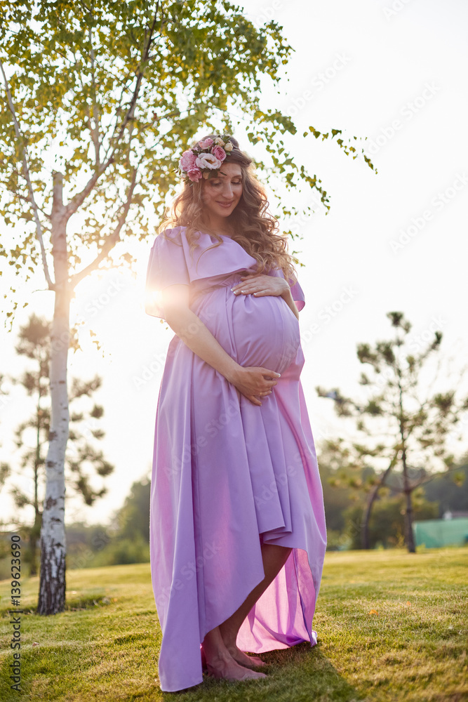 Pregnant woman walks in park at evening. Family enjoying pregnancy. The concept of Mother's Day and Women's Day.