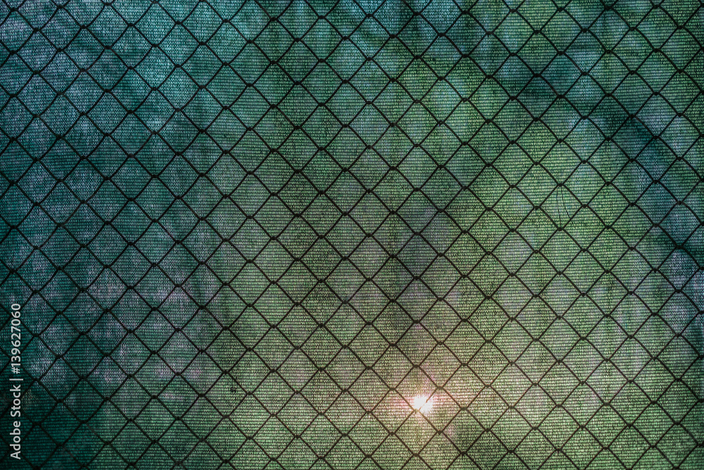Naklejka premium Sun shining through the green net and a fence