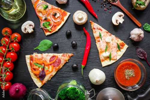 Pizza with ingredients and spices on dark background. Flat lay, top view.