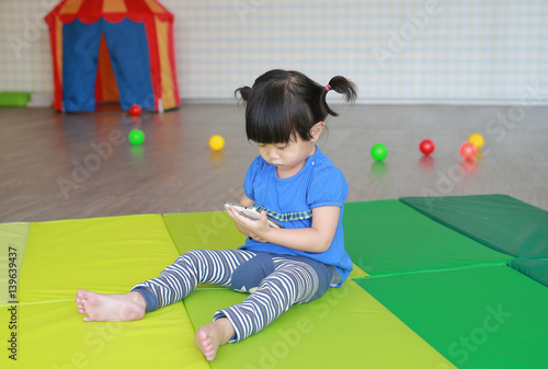 Cute asian baby girl age about one year old and nine month playing a smartphone at the Kid room