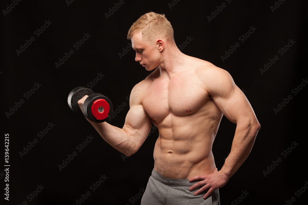 Athletic handsome man fitness-model is working out with dumbbell and showing his perfect body. isolated on black background with copyspace