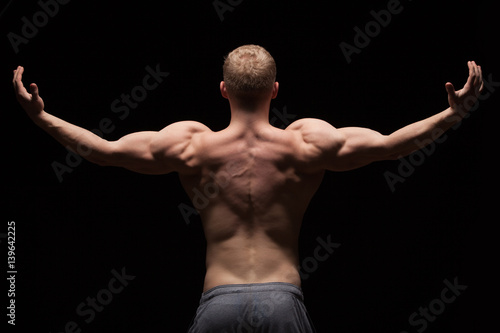 Athletic handsome man fitness-model showing his muscular back, isolated on black background with copyspace