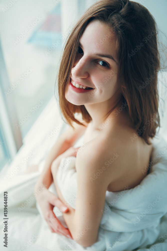 Close up portrait of smiling young beautiful Caucasian woman sitting in bed after waking up, indoors at home early morning, lifestyle, toned with filters Close up portrait of smiling young beautiful Caucasian woman sitting in bed after waking up, indoors at home early morning, lifestyle, toned with filters