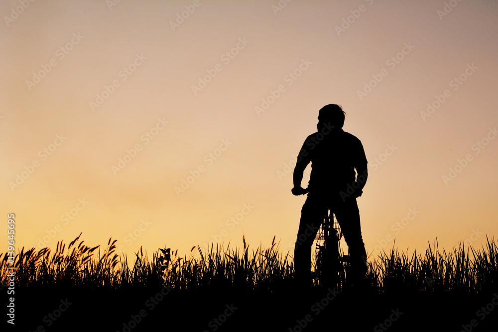 Silhouette of man with bicycle on grass field at the sky sunset, color of vintage tone and soft focus concept journey in holiday