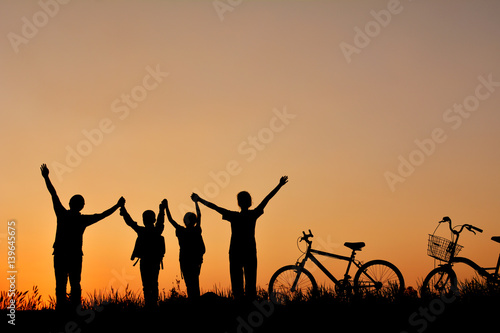 Silhouette of family with bicycle on grass field at the sky sunset, color of vintage tone and soft focus concept journey in holiday