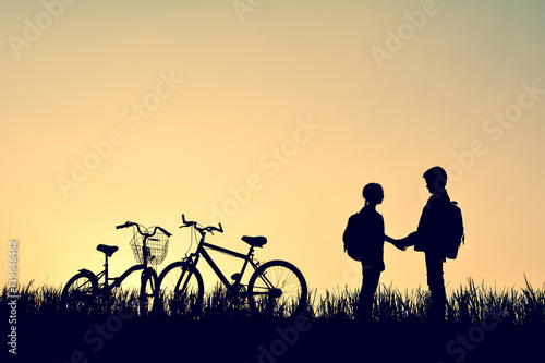 Silhouette of children with bicycel on grass field at the sky sunset, color of vintage tone and soft focus concept journey