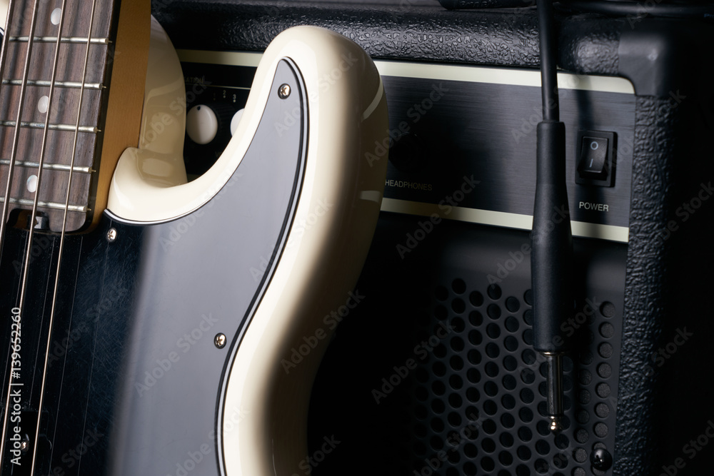 Fototapeta premium Black and white electric bass guitar with jack cable and classic amplifier on a dark background.Close up.