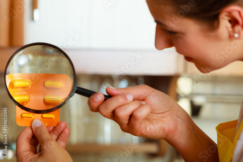 Woman inspecting pills with magnifying glass.