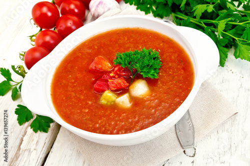 Soup tomato in white bowl with vegetables and parsley on board
