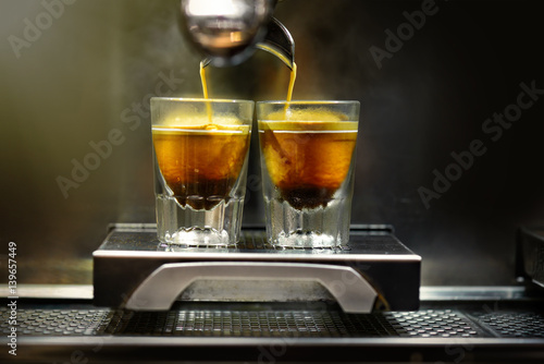 Professional coffee brewing. Coffee espresso. Close-up of espresso pouring from coffee machine to shotglasses. photo