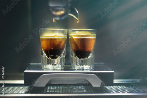 Professional coffee brewing. Coffee espresso. Close-up of espresso pouring from coffee machine to shotglasses. photo