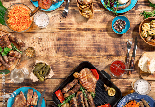 Barbecued steak, sausages and grilled vegetables on wooden picnic table