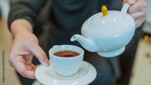 Woman's hands pour hot tea into white cup.