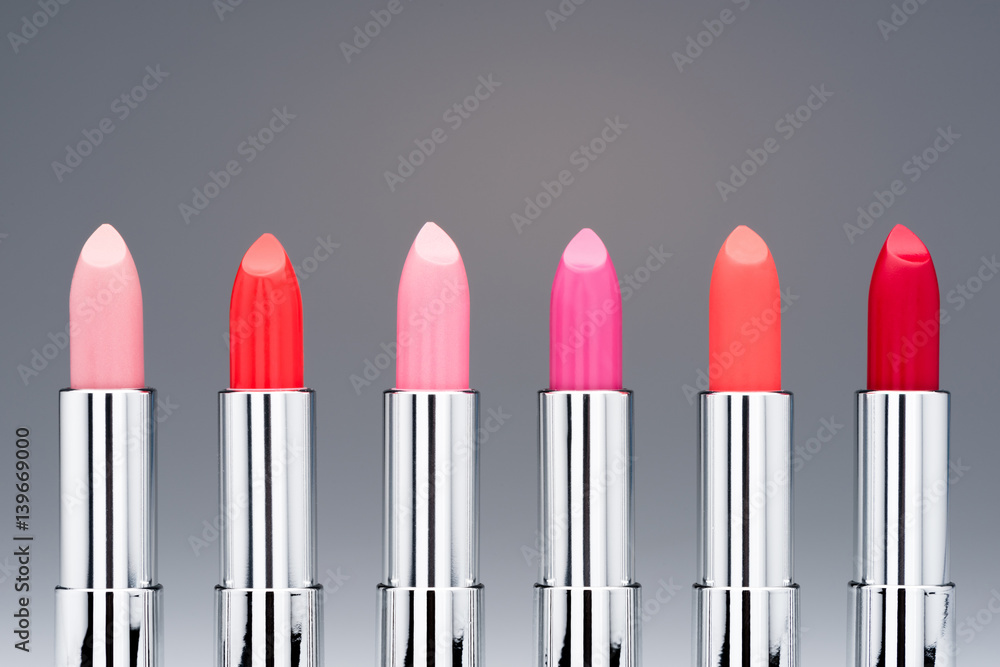 Close-up view of collection of fashionable glossy lipsticks in row on grey Close-up view of collection of fashionable glossy lipsticks in row on grey