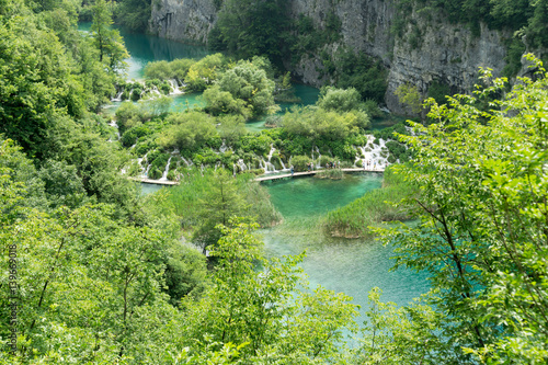 The view overlooking some of the waterfalls and lakes at Plitvice Lakes National Park, with unrecognizable tourists walking along a pathway.