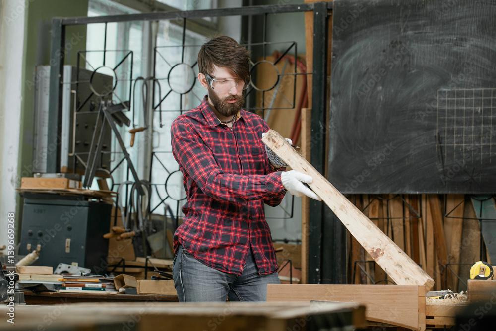 Carpenter examining plank of wood by workbench