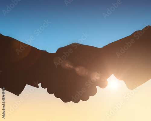 Silhouettes shaking hands against sun shining