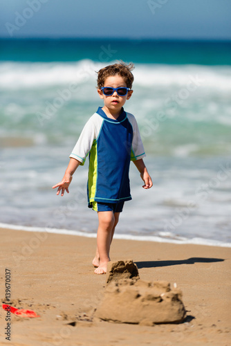 Little boy standing in frot of sand castle photo