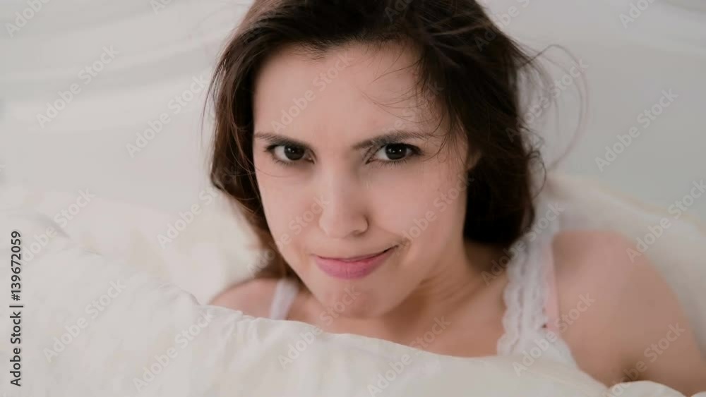 Close-up view of young woman looking at camera, blowing to the hair. Attractive girl hides under the sheet. Close-up view of young woman looking at camera, blowing to the hair. Attractive girl hides under the sheet.