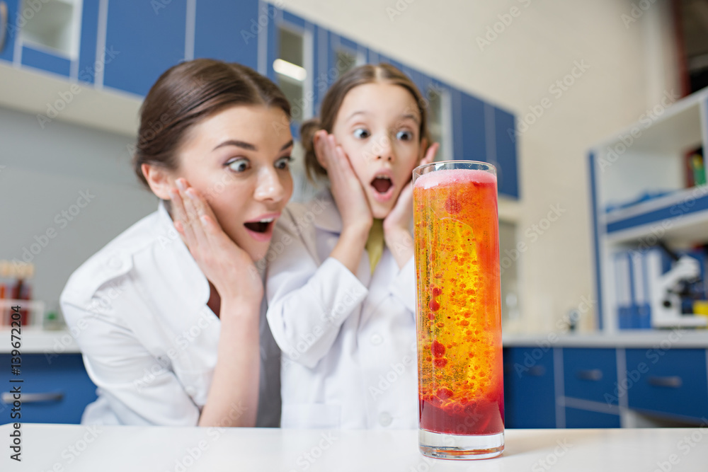 shocked woman teacher and girl student scientists looking at experimental tube in lab shocked woman teacher and girl student scientists looking at experimental tube in lab