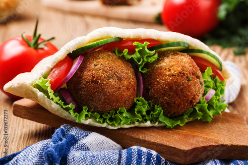 Falafel and fresh vegetables in pita bread on wooden table