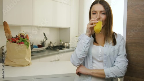 Pretty girl drinking fresh orange juice in the morning in the kitchen. photo