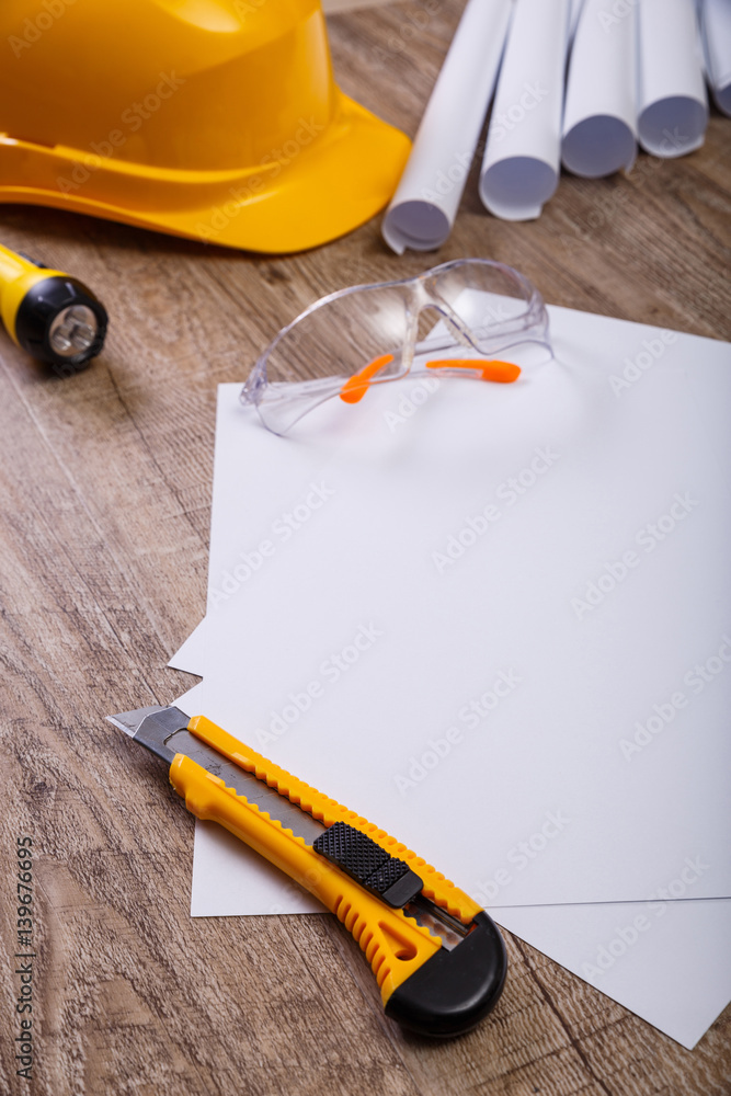 Fototapeta premium Protective glasses and helmet. Flashlight, knife and architecture plans. Blank sheet of paper. Wooden rustic background.