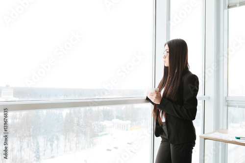 Pensive businesswoman standing and thinking near the window in office