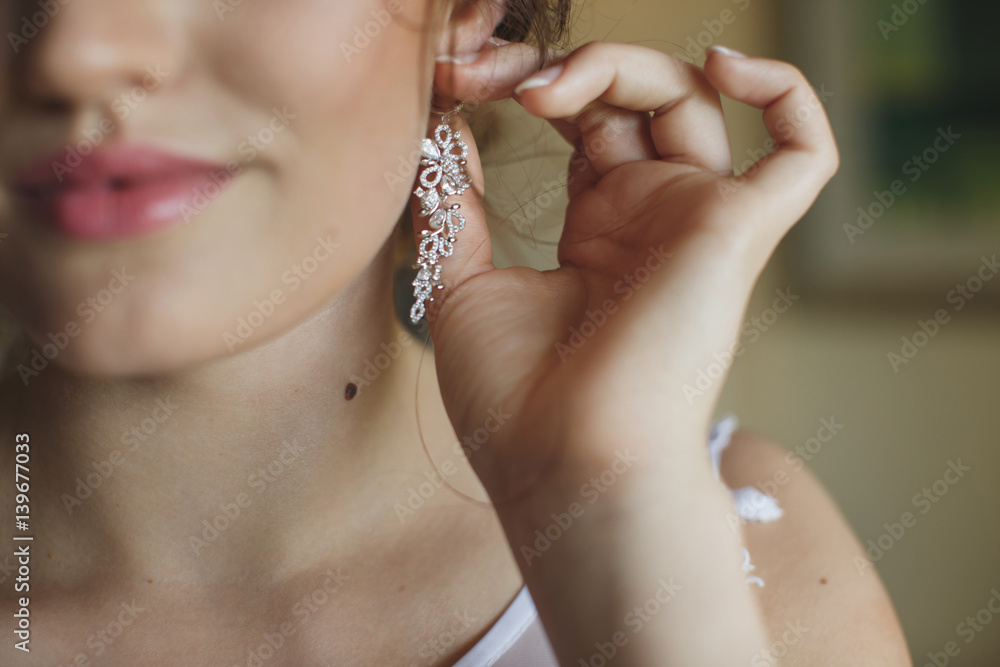 Wedding earrings on a female hand, she takes the earrings, the bride fees, morning bride, white dress, wear earrings